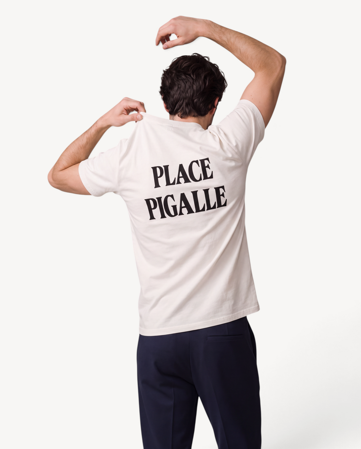 Homme portant un t-shirt Le Comptoir National blanc cassé en coton bio avec l'inscription Place Pigalle au dos