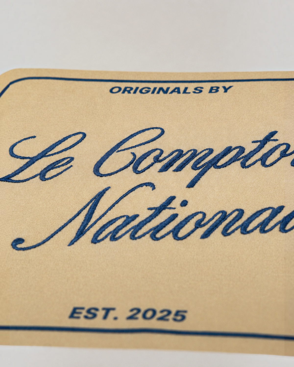 Gros plan sur le logo brodé Originals by Le Comptoir National en bleu sur un t-shirt en coton bio couleur crème