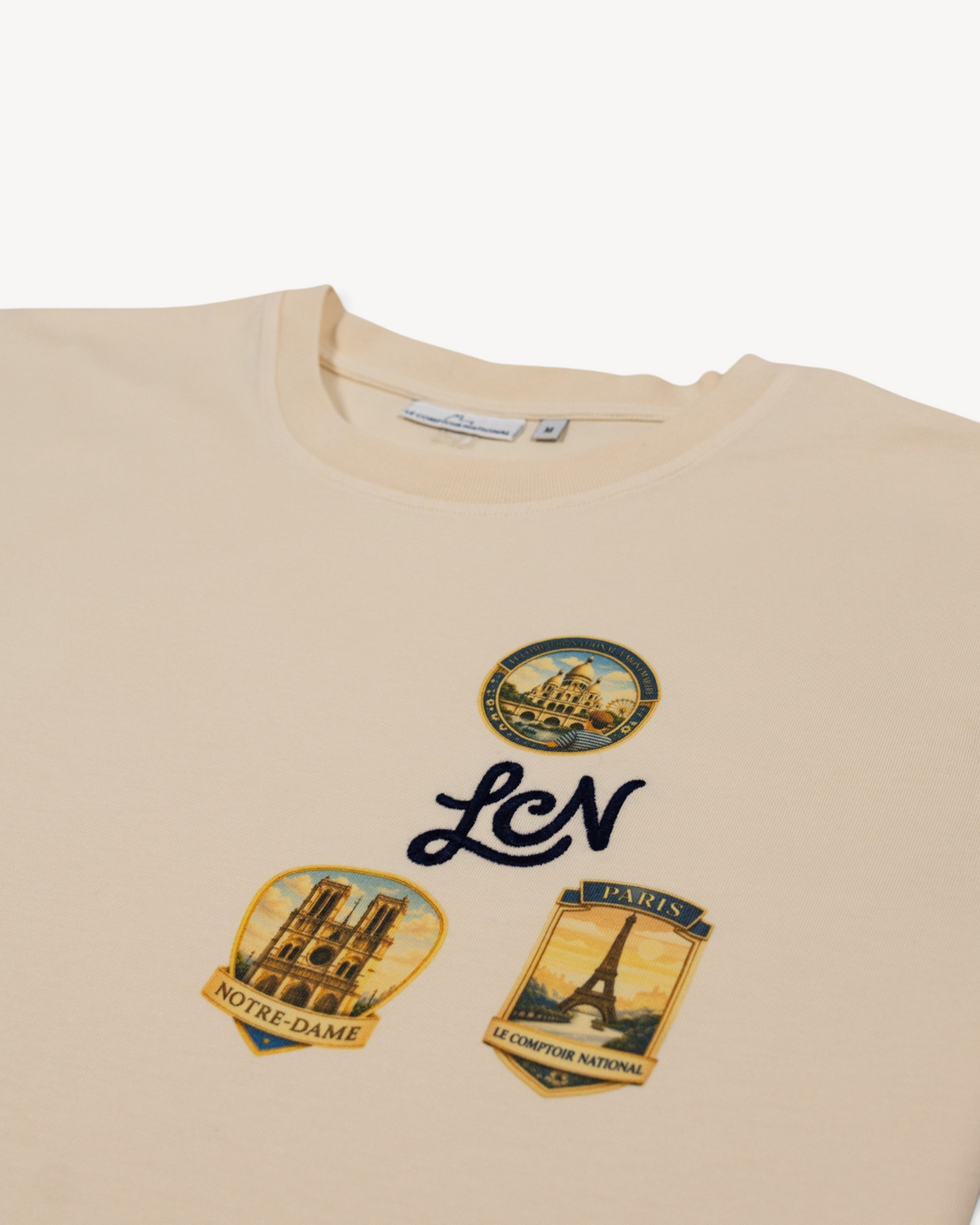 T-shirt Le Comptoir National en coton bio blanc cassé avec trois écussons graphiques de Paris et broderie LCN bleue